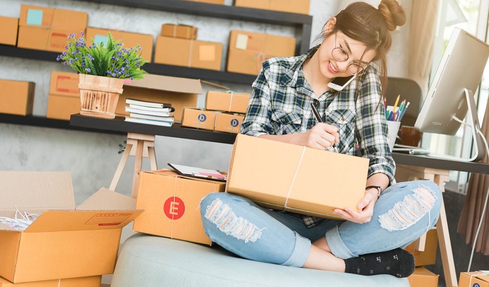 A person sitting on a couch holding a box and talking on a cell phoneDescription automatically generated